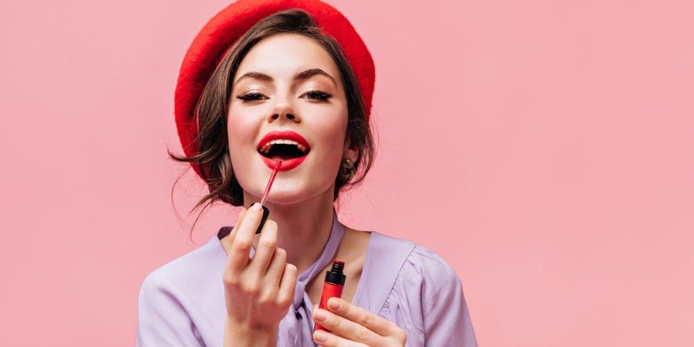 woman-bright-beret-paints-her-lips-with-red-lipstick-girl-lilac-blouse-posing-pink-background